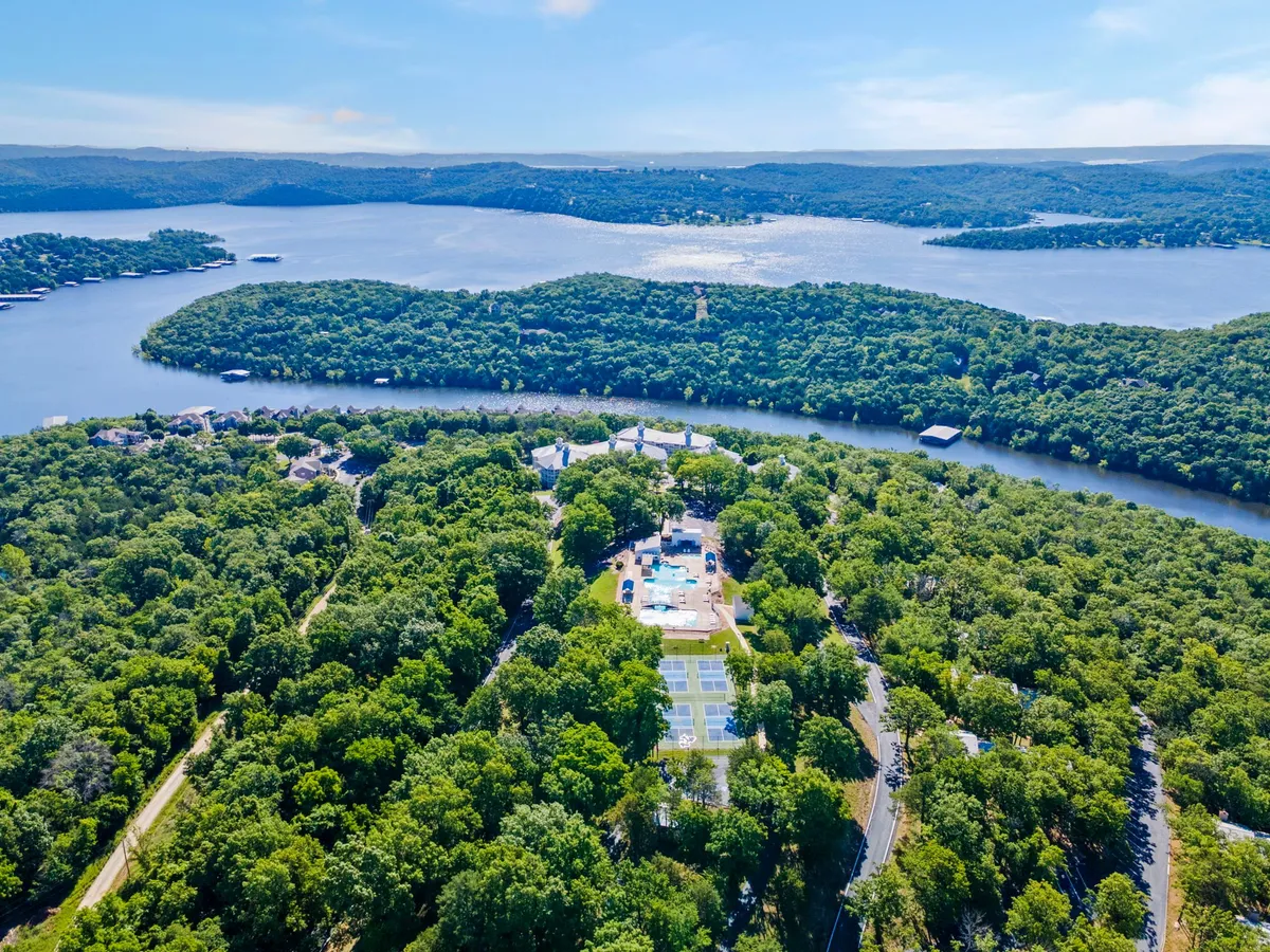 This exterior image features lush green trees, expansive water views of Table Rock Lake, a swimming pool, and tennis courts. The open landscape and nearby nature align with active, outdoor adventures for guests and their pets.