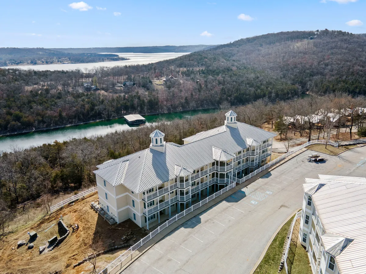 A tranquil exterior view of a lakefront setting, with the building’s architectural details framed by the water and rolling green hills in the background. The scene suggests easy access to outdoor adventures and relaxation.