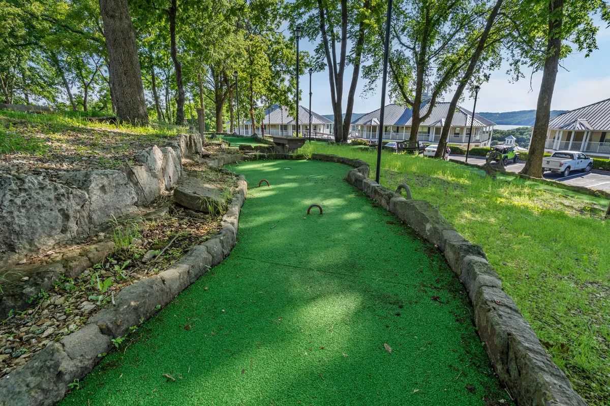 This image showcases a vibrant mini-golf course surrounded by lush greenery and bordered by natural stone, with ample space for groups to enjoy friendly competitions. The joyful and playful atmosphere is ideal for family outings and social gatherings, capturing participants enjoying active outdoor fun.