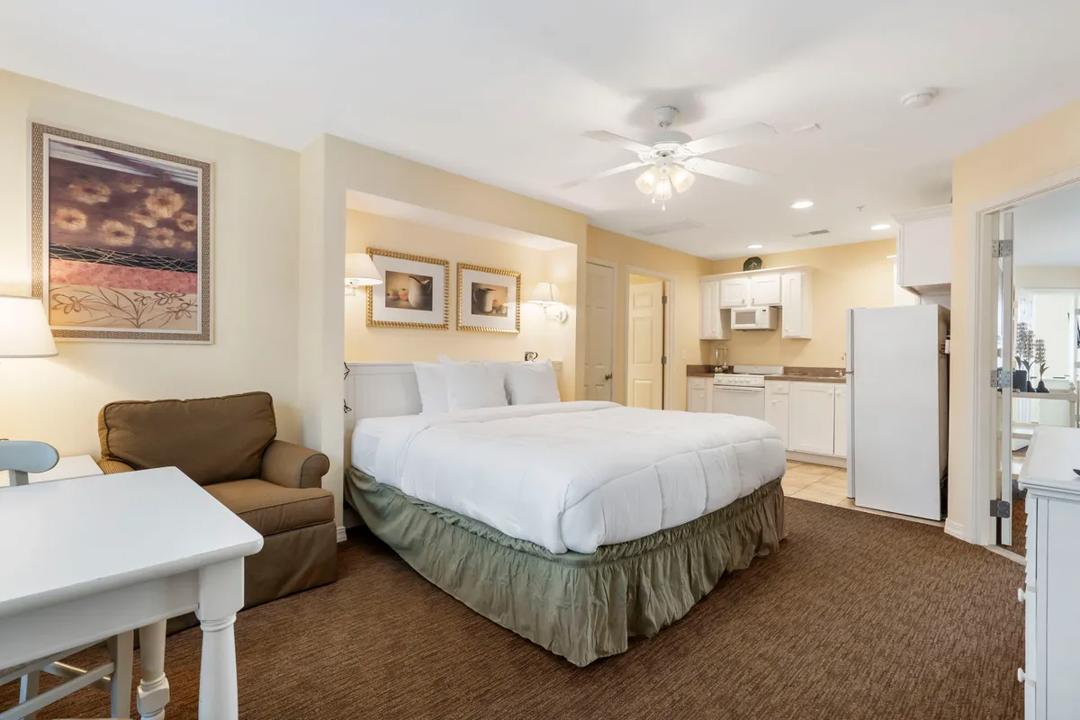 A king-sized bed anchors the room, accompanied by a cozy seating area and a kitchenette thoughtfully arranged along one wall. Soft lighting and subtle décor create a restful, homelike environment, while the kitchenette includes a mini fridge, microwave, and sink—perfect for preparing snacks or enjoying an independent stay.