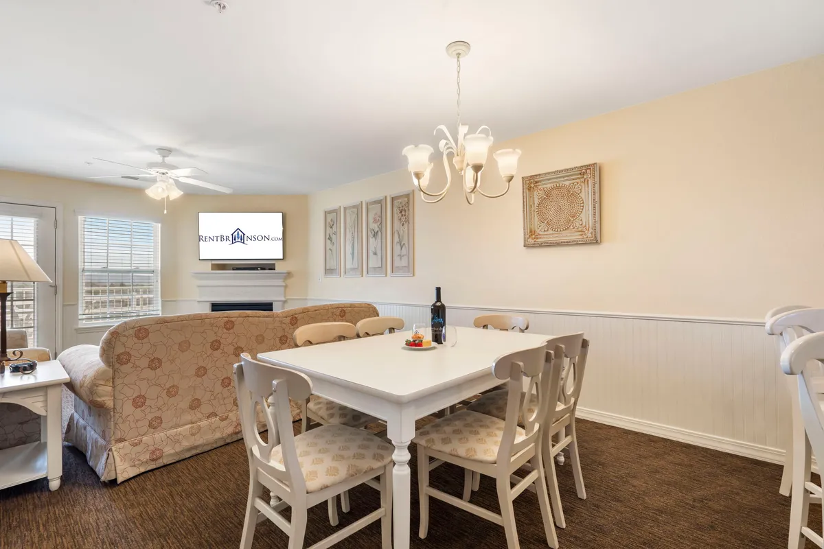 A warm, inviting interior scene showing a dining table and comfortable seating area, illuminated by a chandelier. The space is designed for family dinners, game nights, or relaxing after a day of activities, embodying the comfort and spaciousness described in the condo accommodations.