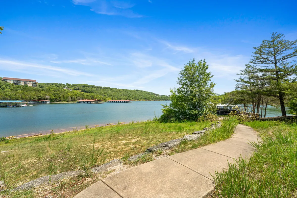 A tranquil view across a lakeside pathway bordered by trees and gentle hills in the background. The peaceful scene invites guests and their furry companions to stroll, fish, or simply enjoy nature by the water.