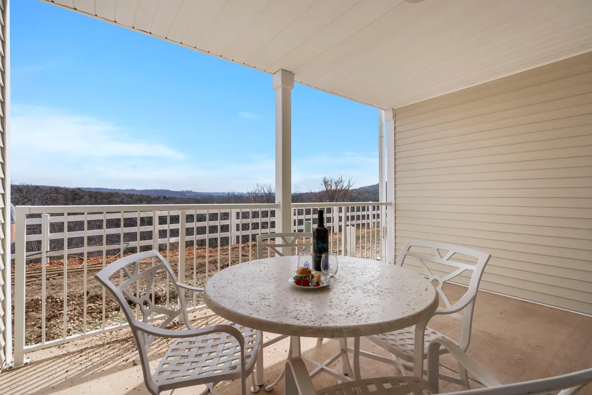 An inviting outdoor deck scene featuring a table set for two with wine and fruit, overlooking a scenic landscape. Comfortable seating suggests it's a perfect spot for couples to relax, enjoy a meal, or sip morning coffee while surrounded by nature.