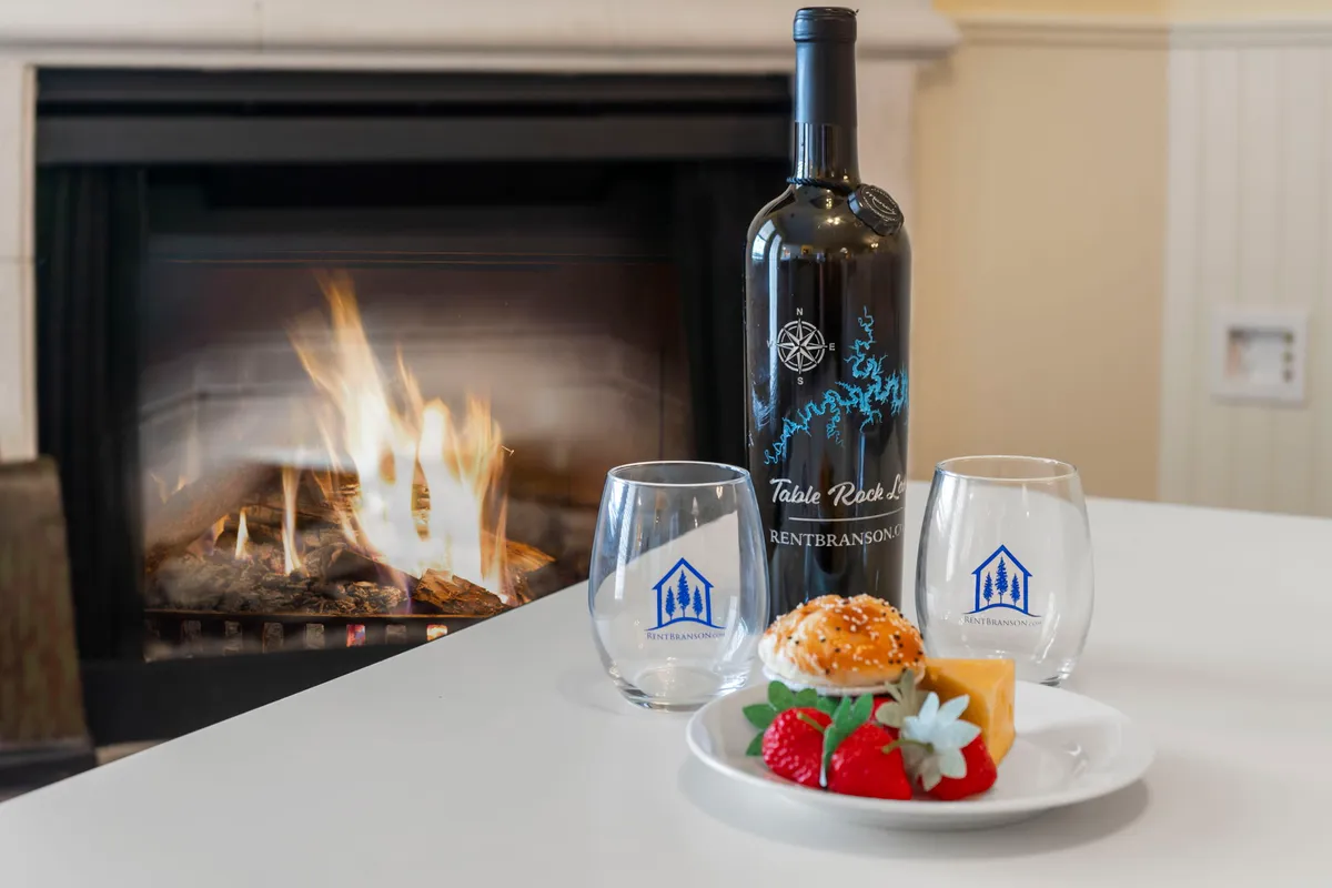 A cozy interior scene with a bottle of wine and glasses set on a table, gourmet dessert, and a fireplace in the background. The warm lighting and intimate arrangement invite couples to unwind together indoors, perhaps after a day of local exploration.