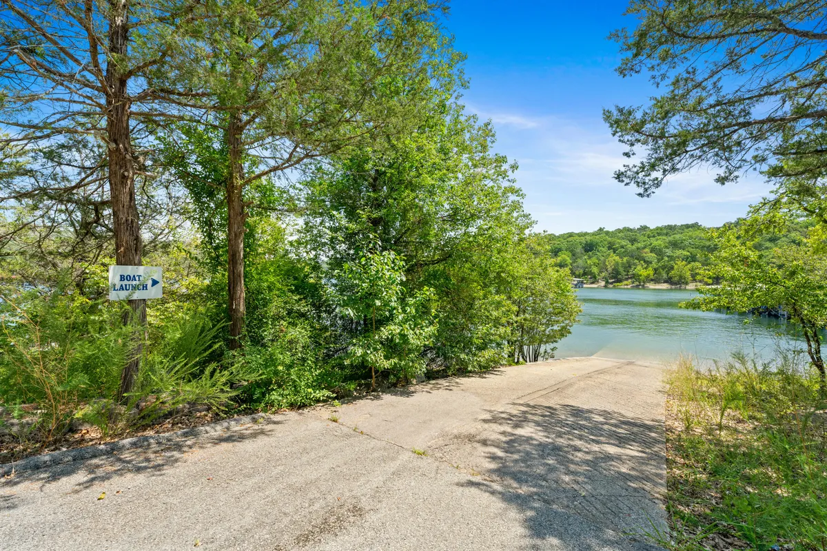 A boat launch area with a clear sloped concrete path leading down to the water, framed by greenery, with a visible sign indicating the boat ramp. The scene suggests ease of access to the lake for boating and fishing adventures.