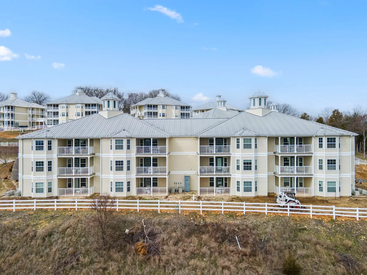 An exterior scene showing the resort's building structure with balconies overlooking the surrounding landscape. The environment includes open green areas and paths, evoking a sense of community and connection with nature.