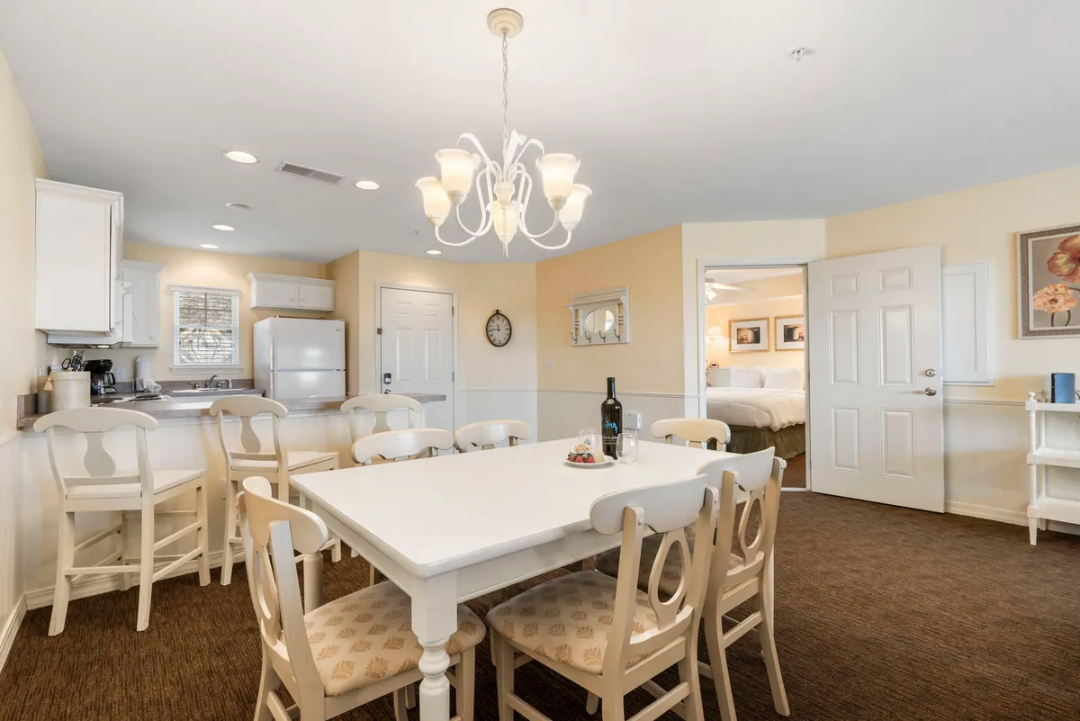 A warm, inviting dining area with a central table, chandelier, and views into the kitchen space. Decorative items on the table and doorways leading to other rooms emphasize the multi-use nature of the area.