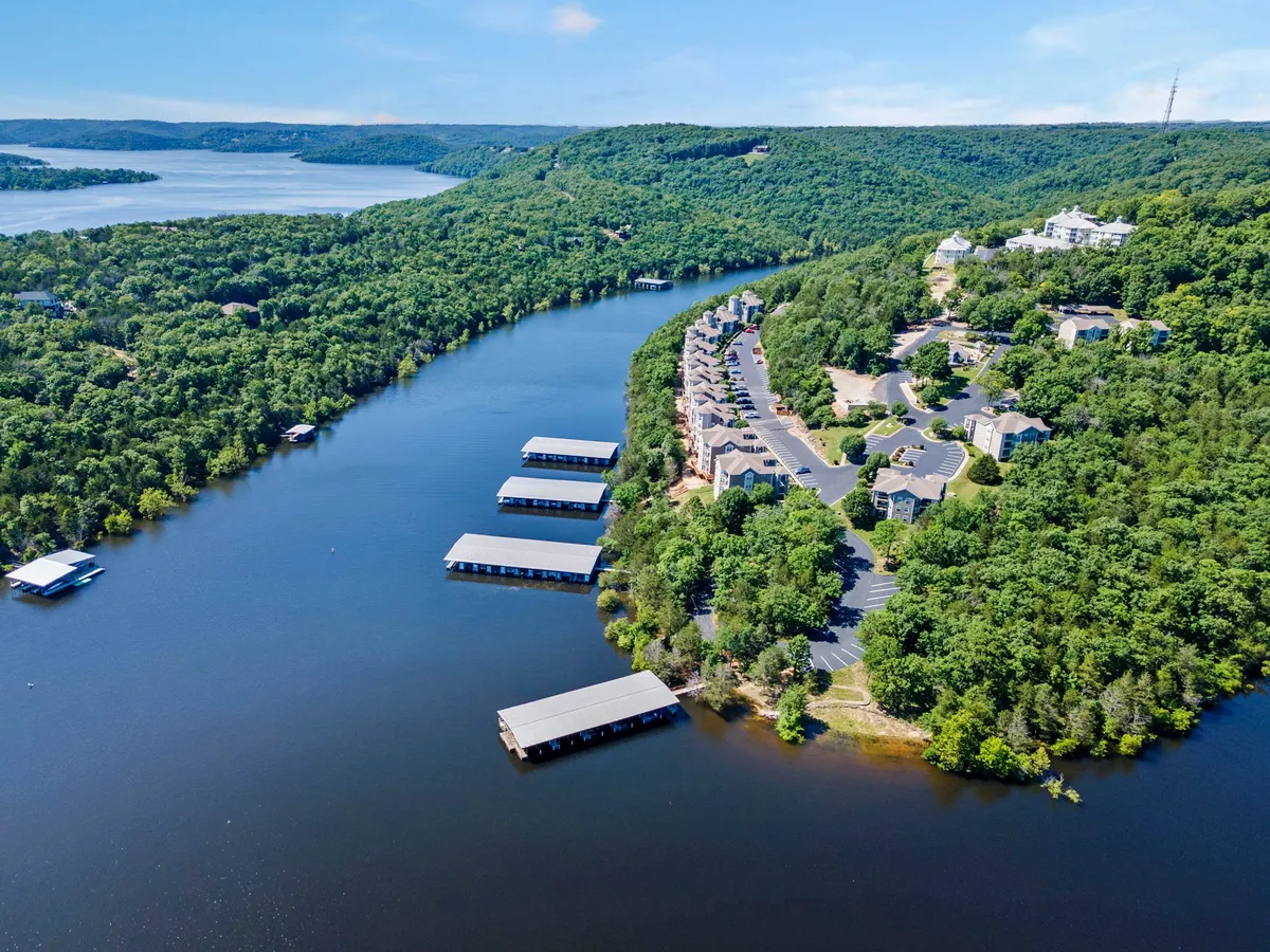 A peaceful scene with the lake, docks, surrounding green hills, and residential buildings in the background. The setting is ideal for leisurely walks along the shore or enjoying time outside with pets.