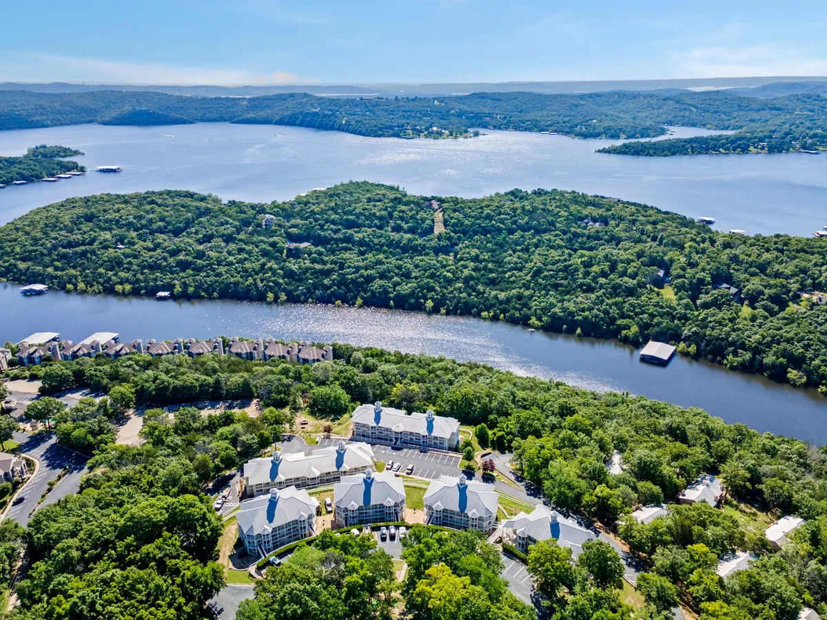 A wide, scenic view over an expansive lake, encircled by lush greenery and a cluster of resort buildings. The natural beauty and recreational possibilities of the area are on full display.