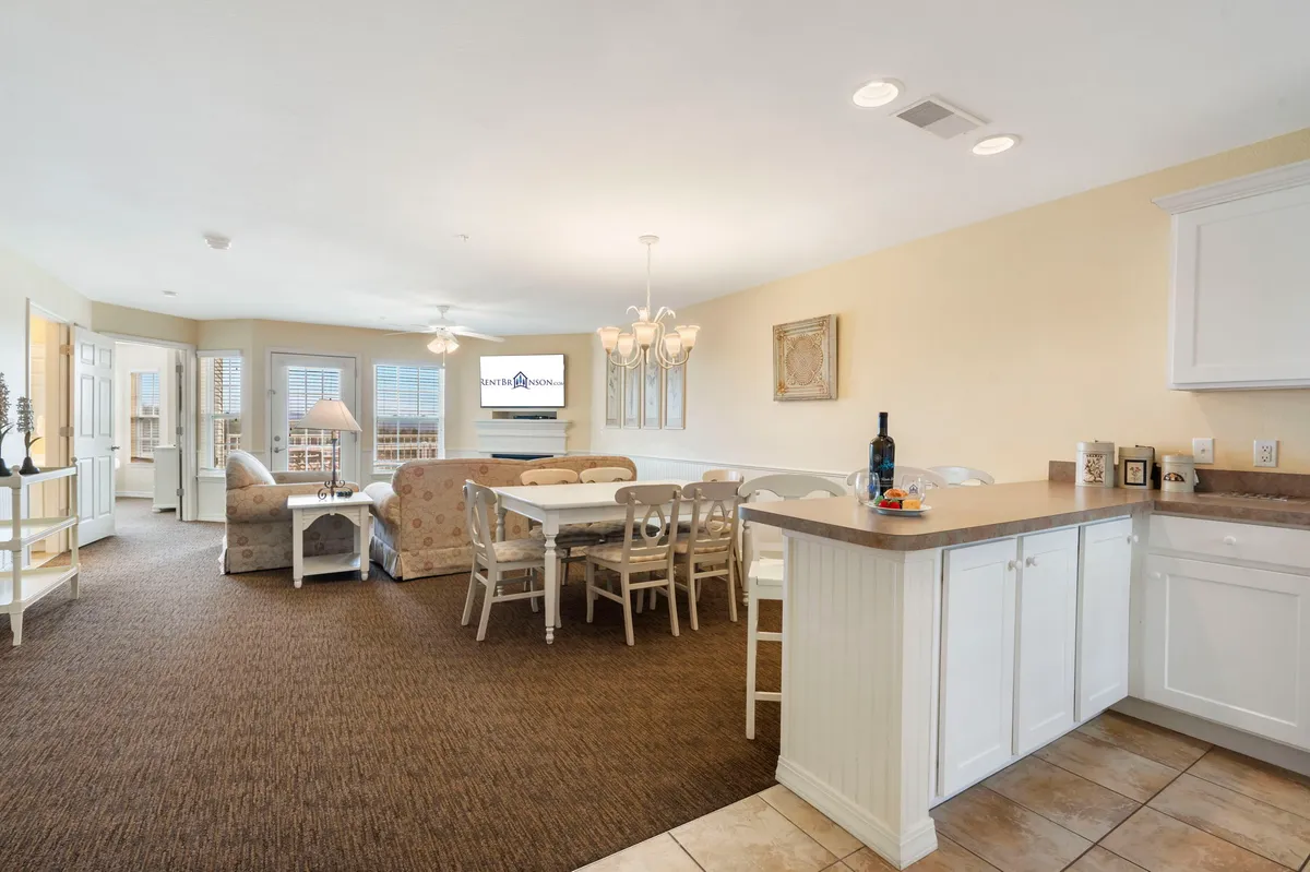 A wide shot integrating the dining table, kitchen counter, and living area seating, all unified by a central chandelier. The open layout facilitates seamless movement and interaction between spaces, embodying the open-concept design described.